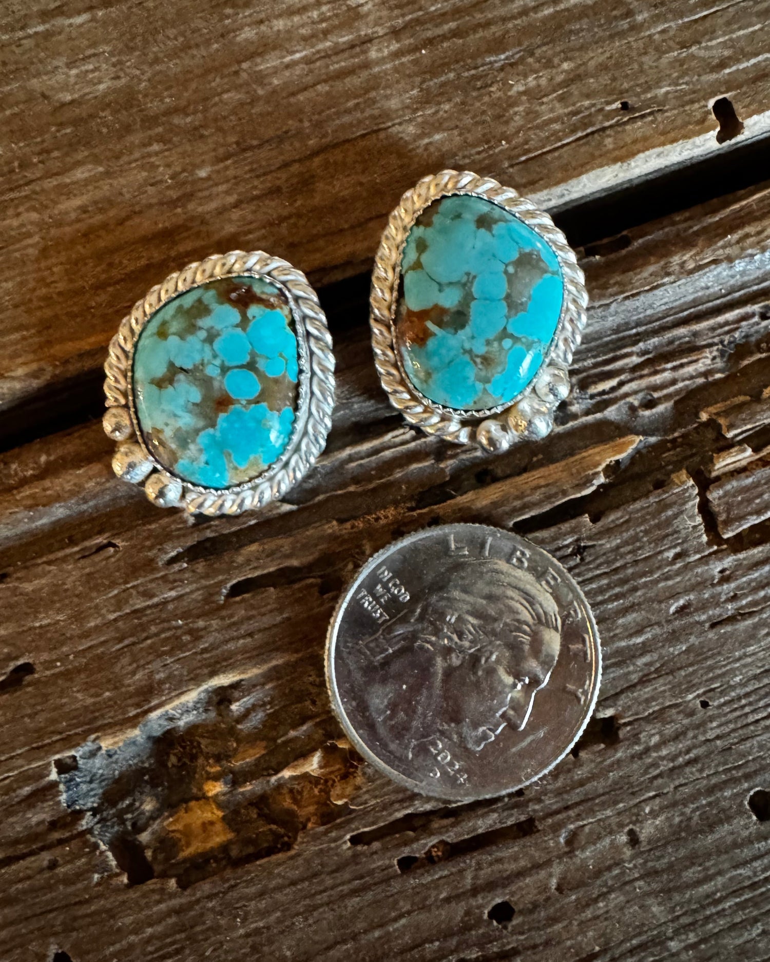 Turquoise stone earrings on a wooden surface with a coin for scale.