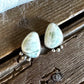 Tear-shaped light green gemstone stud earrings with silver settings and small dangling silver beads, displayed on a rustic wooden surface with a white faux fur accent.