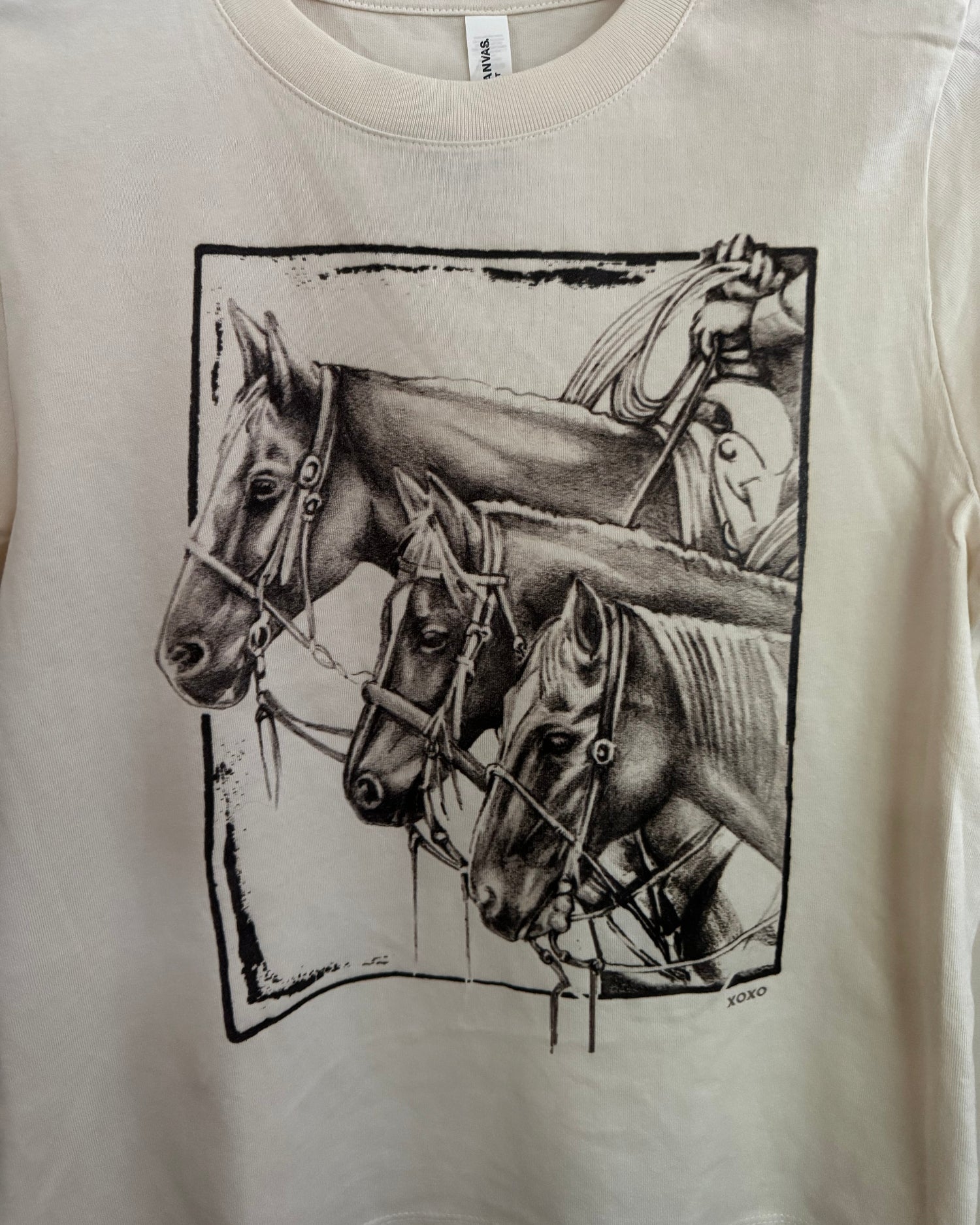White shirt with black graphic design of a horse and rider on a beige background