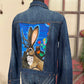 Denim jacket with a painted rabbit design on the back, displayed on a mannequin against a neutral background.
