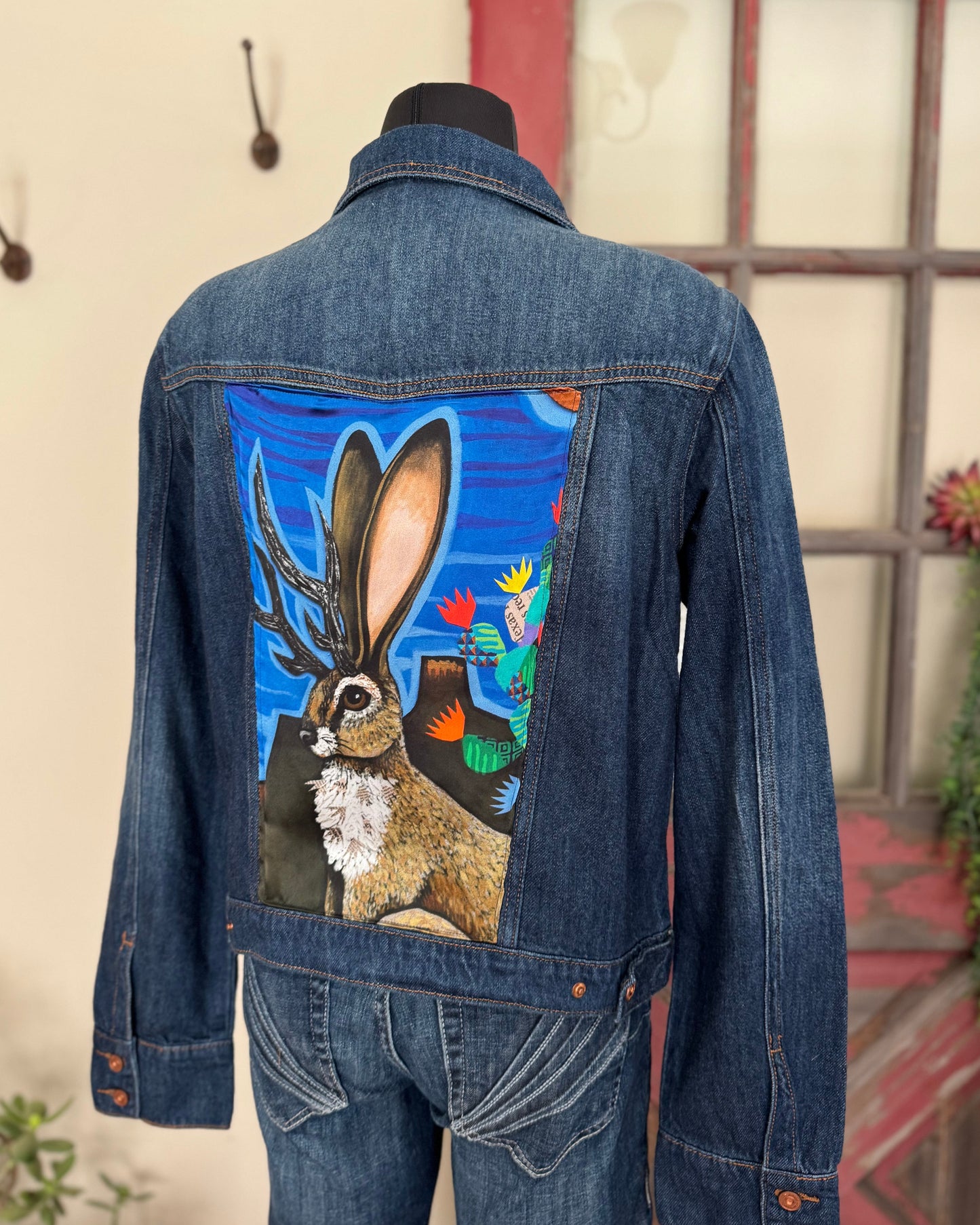 Denim jacket with a painted rabbit design on the back, displayed on a mannequin against a neutral background.