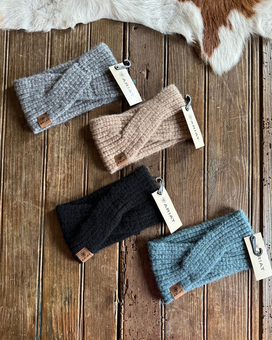 Four knitted headbands in different colors on a wooden surface with Ariat tags.