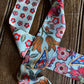 A light blue necktie with a dense floral and paisley print in red, pink, orange, and blue, laid flat on a dark wood background.