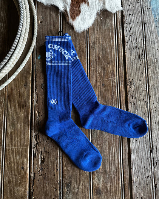 Blue socks with white branding on a wooden surface next to a cowhide rug and rope.