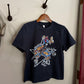 Navy blue t-shirt with graphic design on a wooden hanger against a white wall.