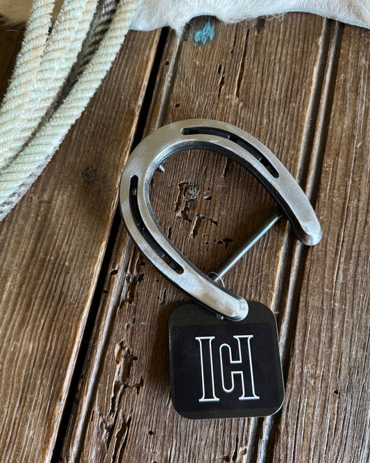 Horseshoe-shaped belt buckle with brand logo on a wooden surface