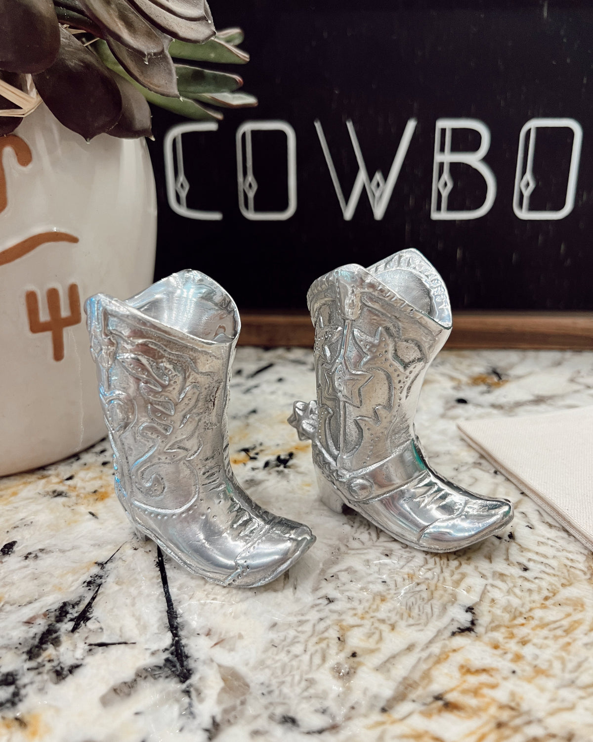 Silver cowboy boot decorations on a marble surface with a chalkboard in the background.