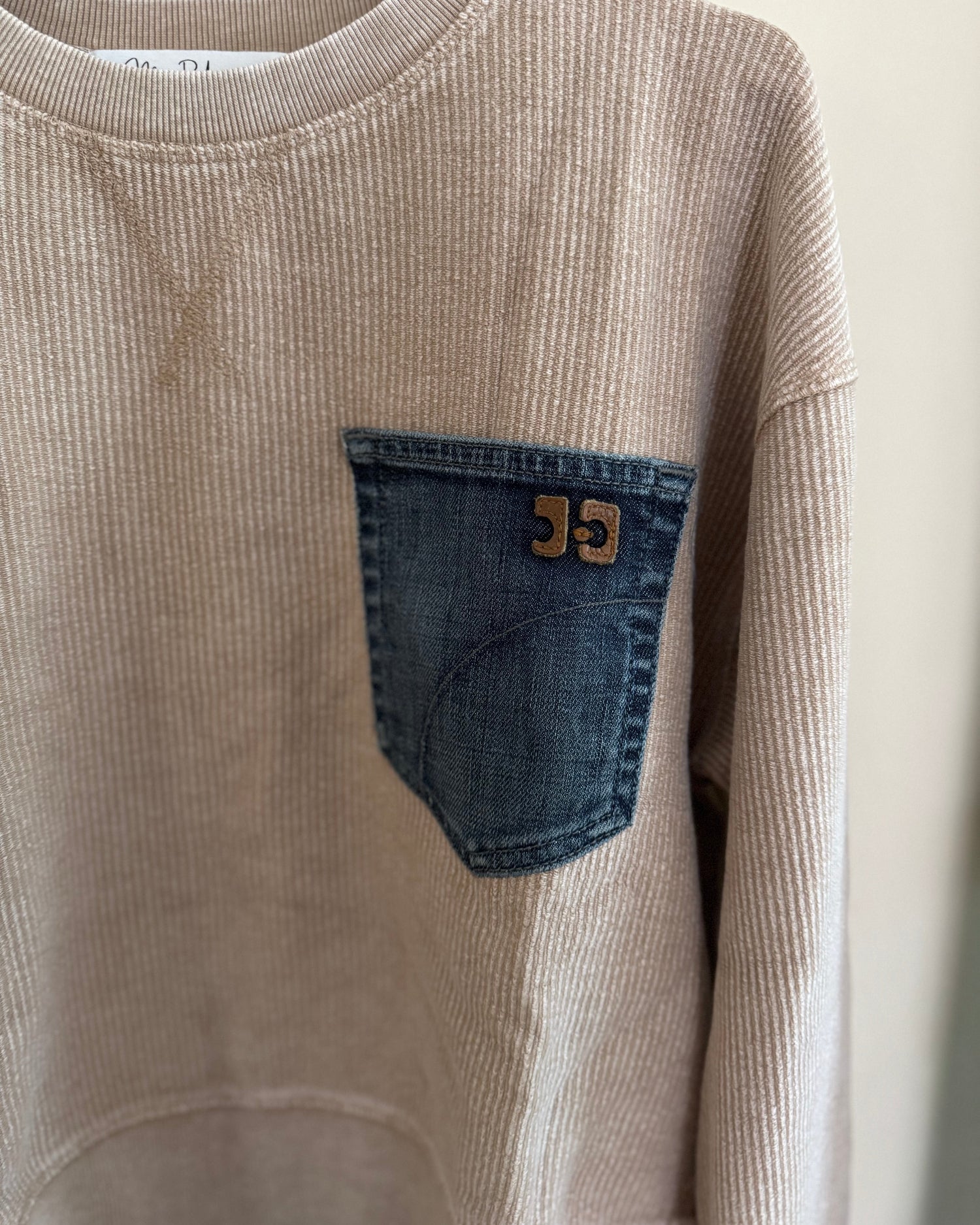 Beige corduroy sweatshirt with a blue denim pocket on a white background