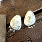 A pair of handmade stud earrings with irregular light green stone pieces in silver settings, shown on a rustic wooden surface next to a metal ruler for scale.