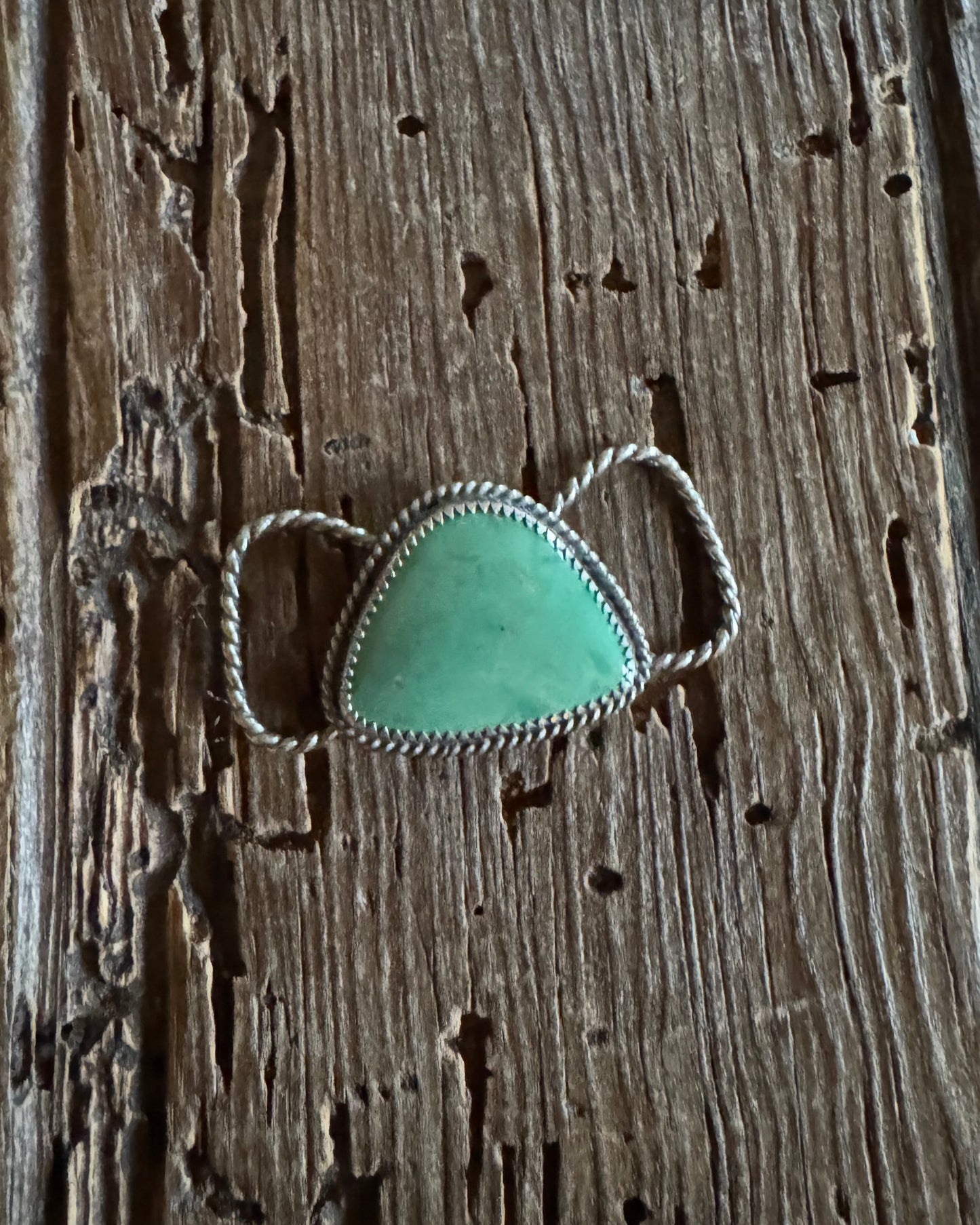 Turquoise teardrop twilly pendant with silver setting on a wooden surface