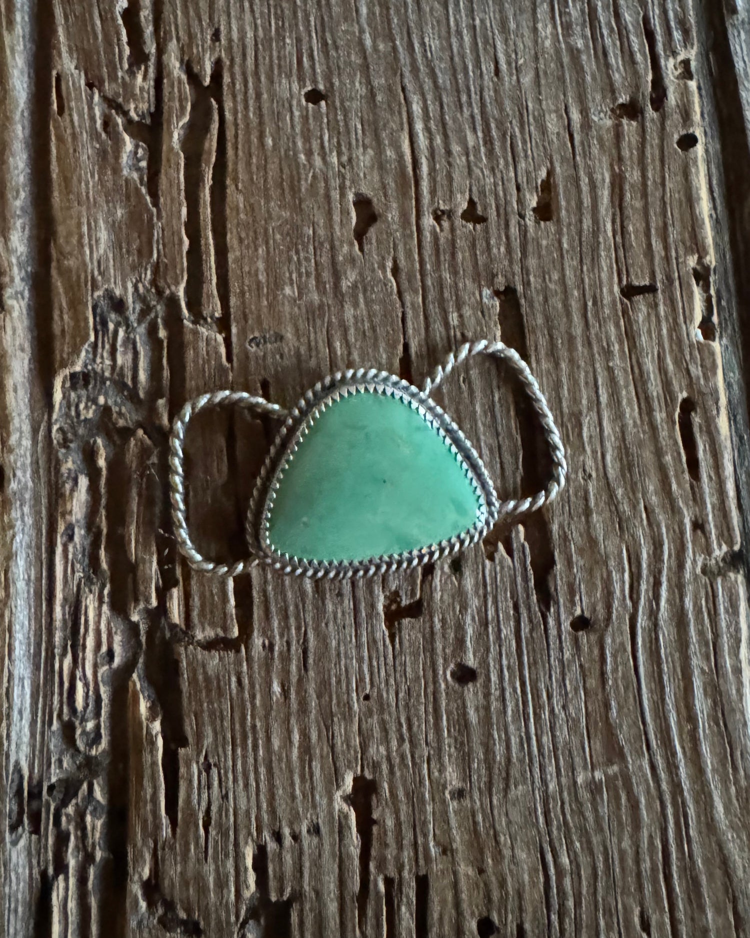 Turquoise teardrop twilly pendant with silver setting on a wooden surface