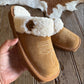 Brown slipper with white fur lining held by a hand on a wooden floor.