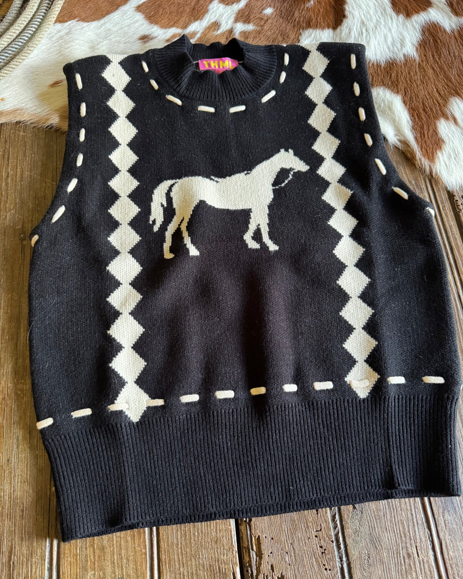 Black sweater with white geometric pattern and horse design on a wooden surface