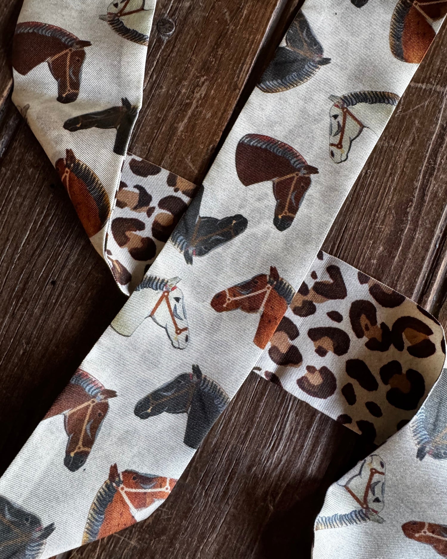 close up of leopard and horse print twilly scarf on a wooden background