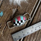 Checkered pendant on a wooden surface with a ruler for scale