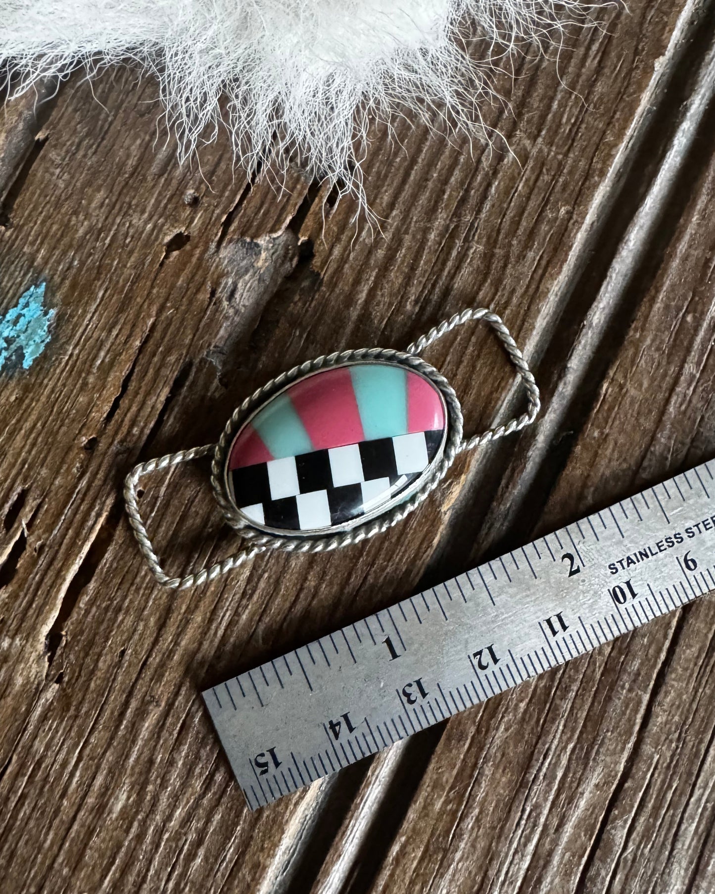 Checkered pendant on a wooden surface with a ruler for scale