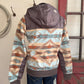 mannequin wearing a patterned jacket with a hood, standing against a wall with a window.