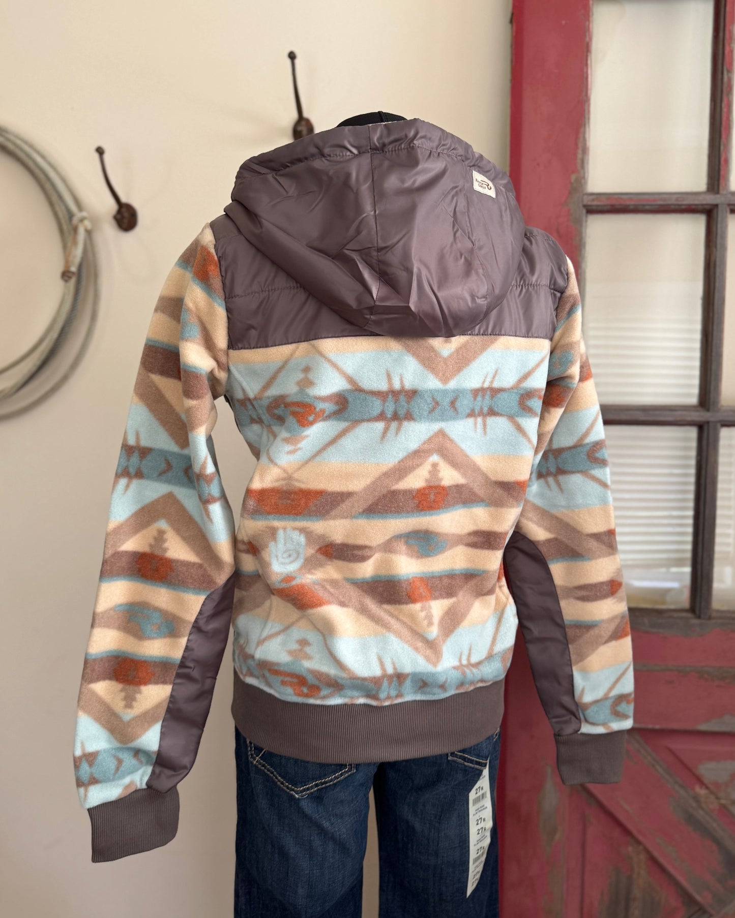 mannequin wearing a patterned jacket with a hood, standing against a wall with a window.