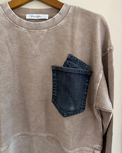 Beige ribbed sweater with a blue pocket on a hanger against a white background