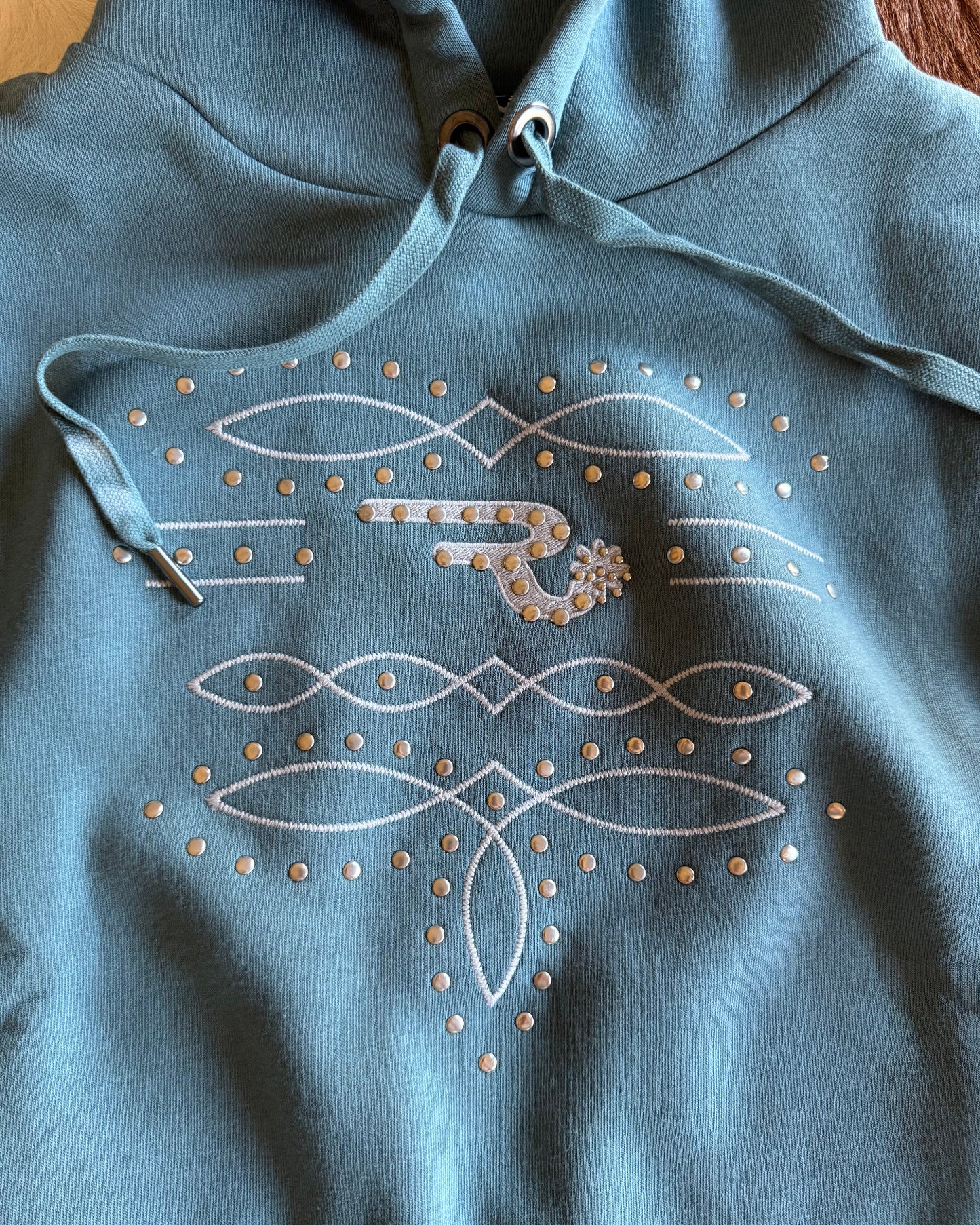 Blue hoodie with white embroidered designs on a wooden surface