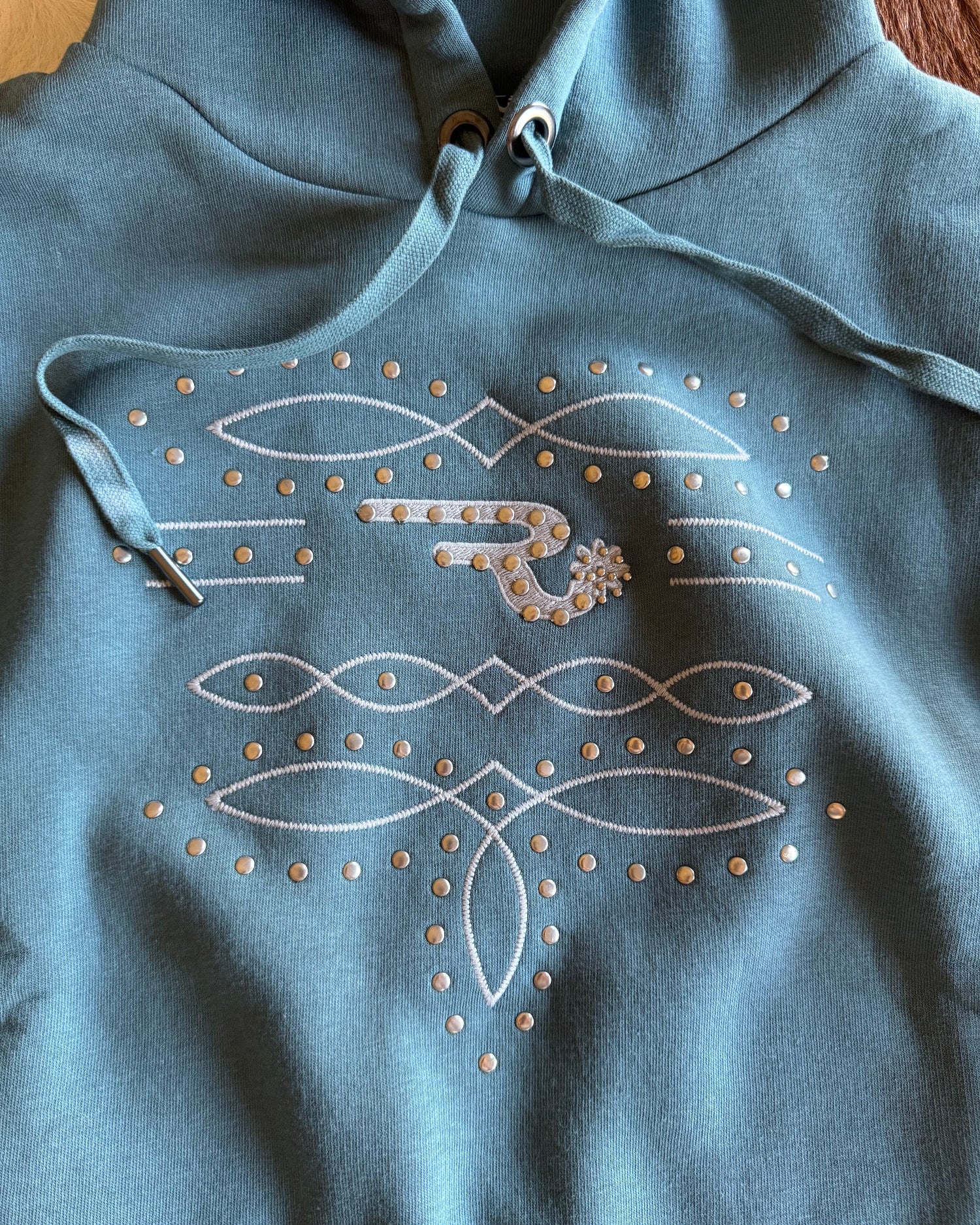 Blue hoodie with white embroidered designs on a wooden surface