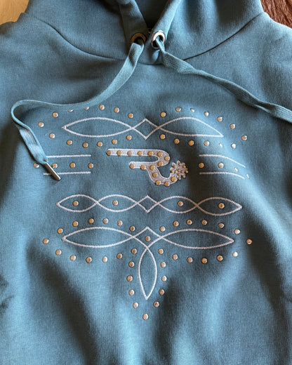 Blue hoodie with white embroidered designs on a wooden surface