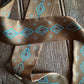 Brown ribbon scarf with blue geometric pattern on a wooden surface