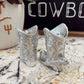 Silver cowboy boot salt and pepper shakers on a marble surface with a 'Cowboy' sign in the background.