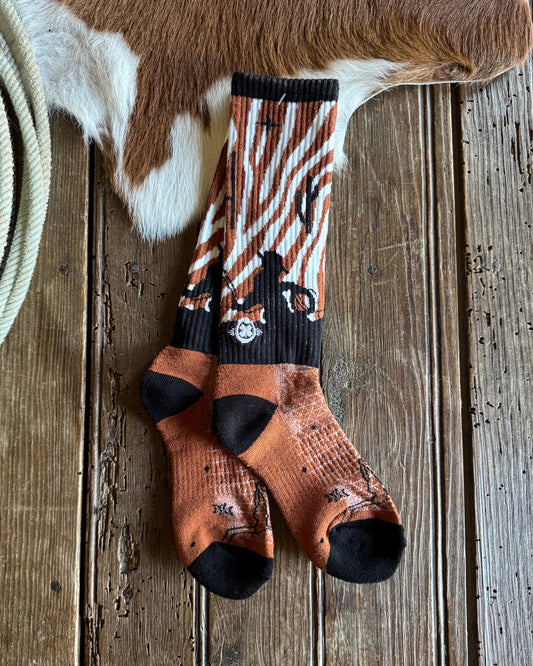 Pair of patterned socks on a wooden surface with cowhide leather and rope.