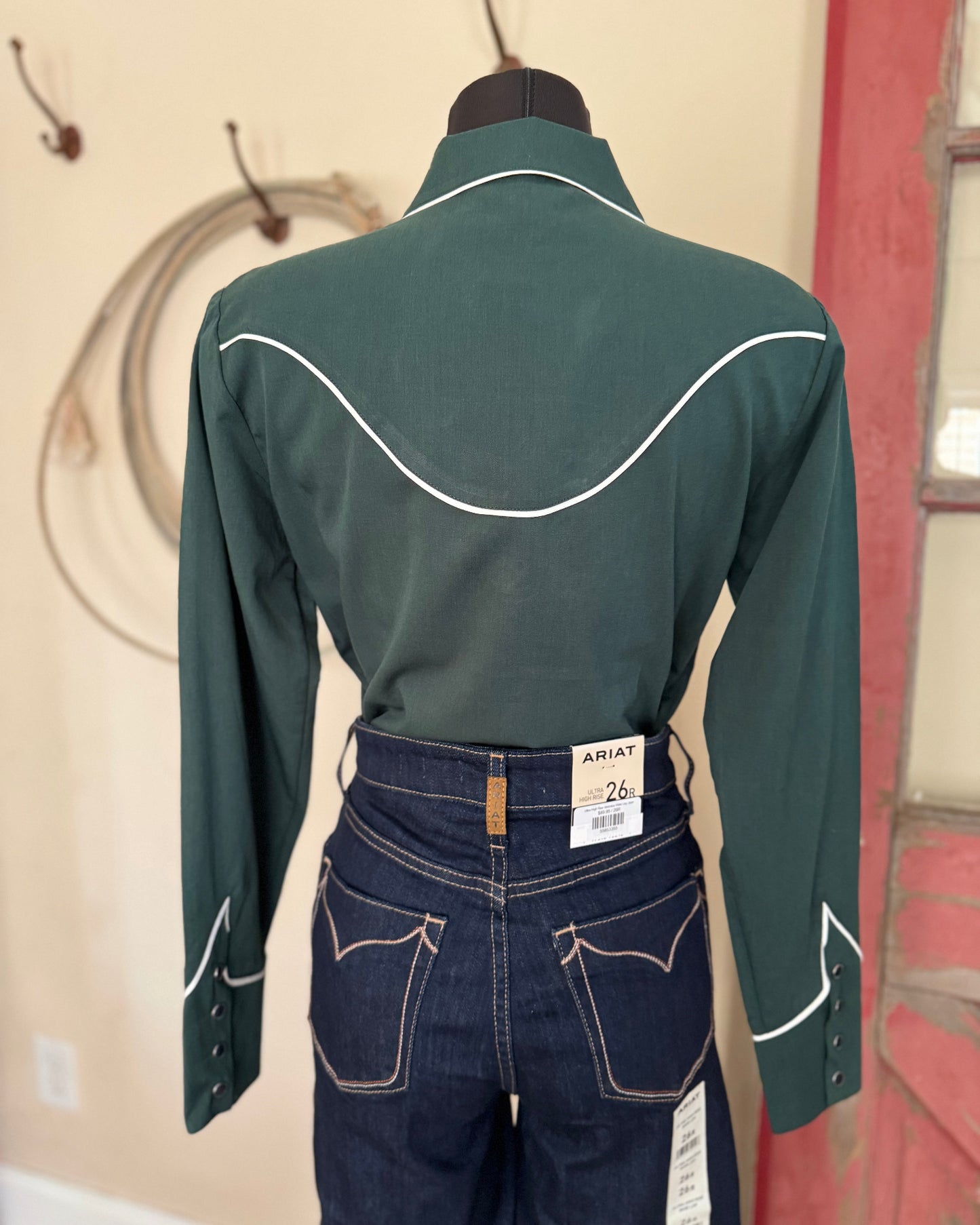 Green long-sleeve shirt with white stitching on a mannequin against a red and beige wall.