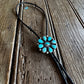 Turquoise flower-shaped pendant on a black cord against a wooden background