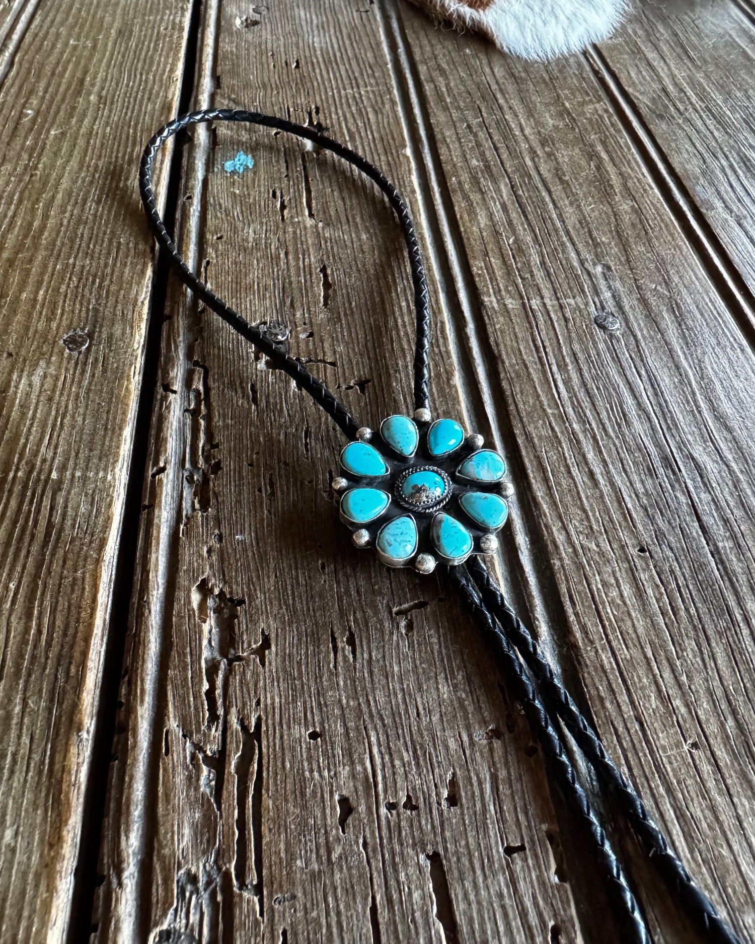 Turquoise flower-shaped pendant on a black cord against a wooden background