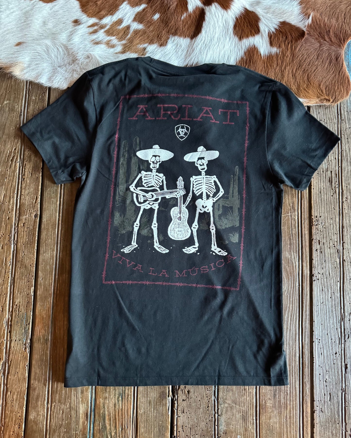 Black t-shirt with skeleton design and 'Ariat' branding on a wooden surface.