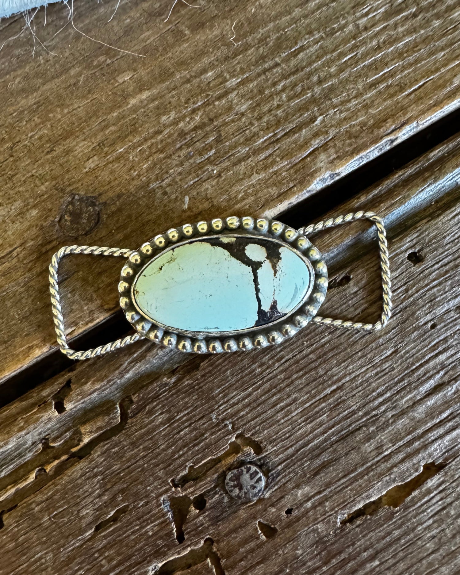 twilly slide with a turquoise stone on a wooden surface