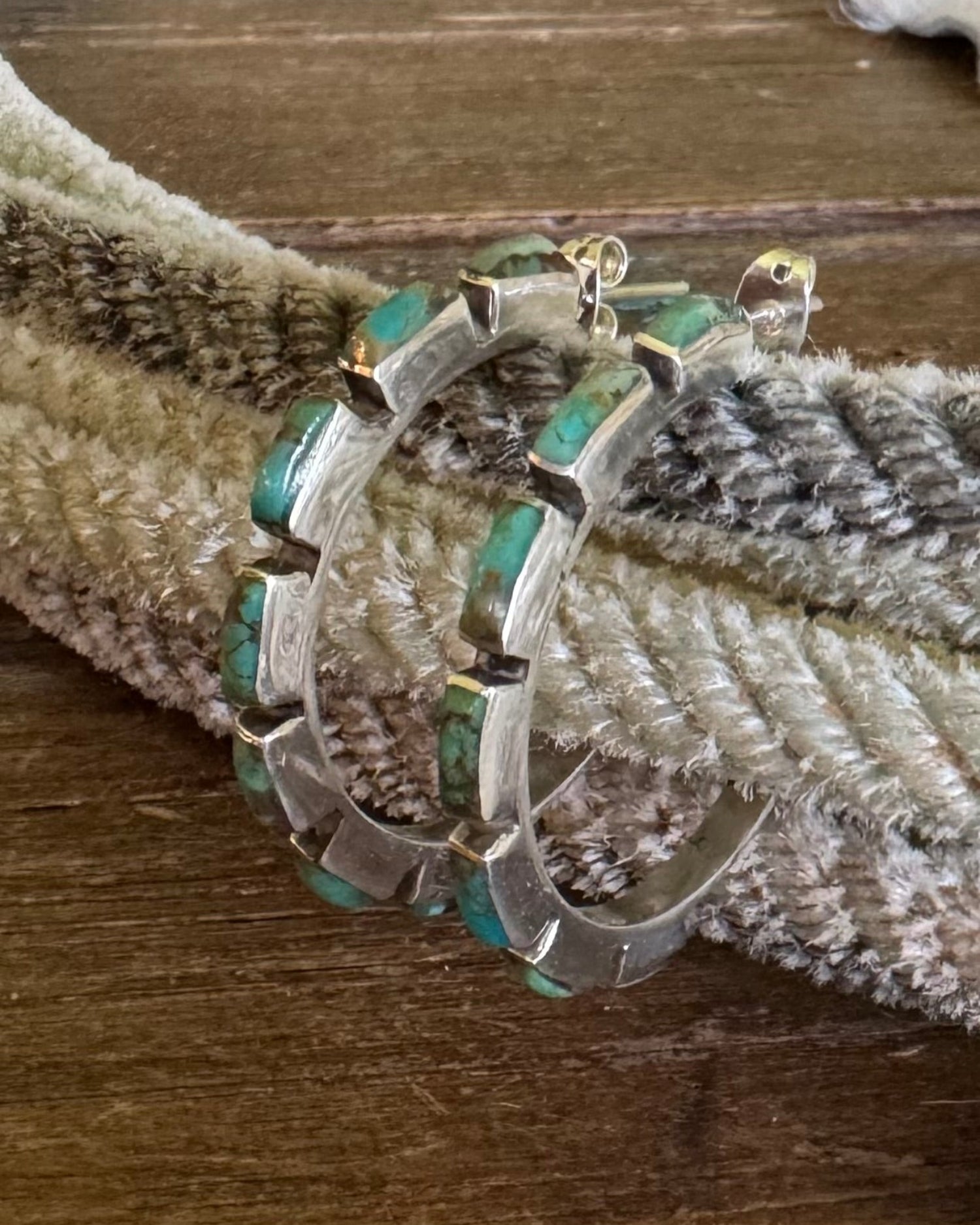 Silver hoop earrings with turquoise stones on a textured surface