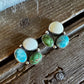 A pair of silver stud earrings with oval turquoise and green cabochon stones, displayed on a rustic wooden surface.