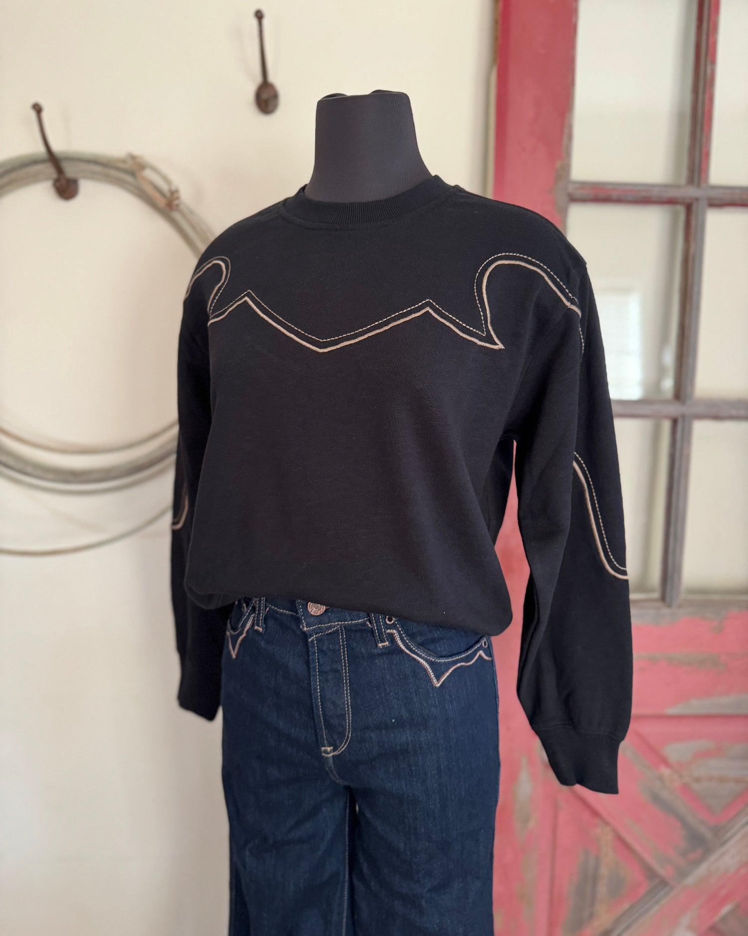 Black sweater with white stitching on a mannequin against a neutral wall.