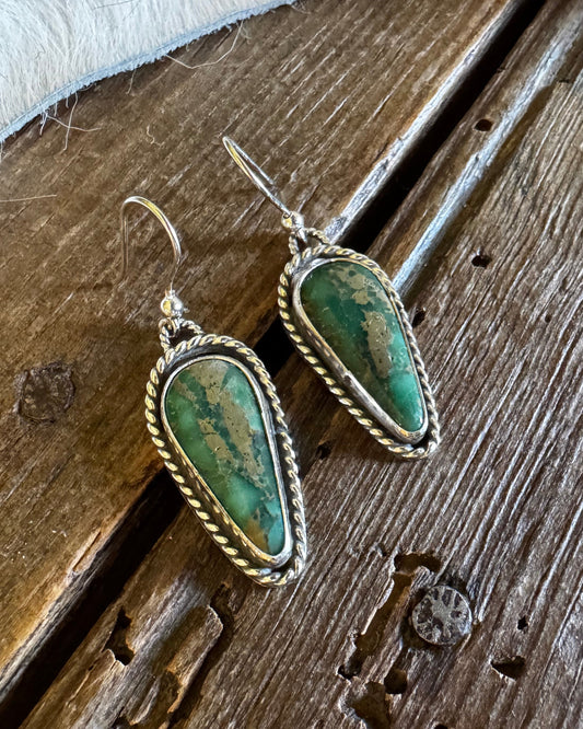 Pair of green stone earrings on a wooden surface