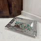 Silver bracelet with turquoise stones on a decorative silver tray against a wooden and marble background