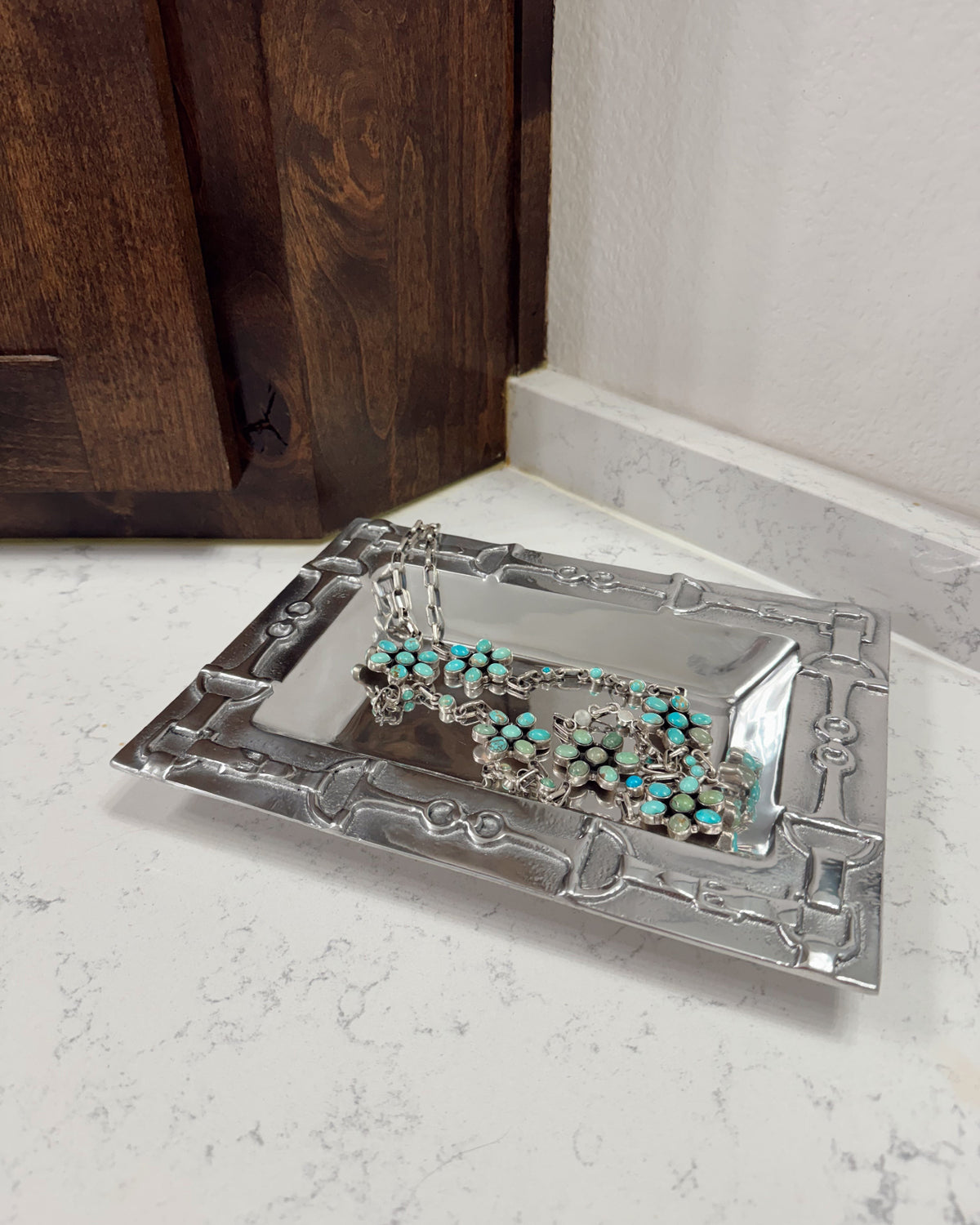 Silver bracelet with turquoise stones on a decorative silver tray against a wooden and marble background