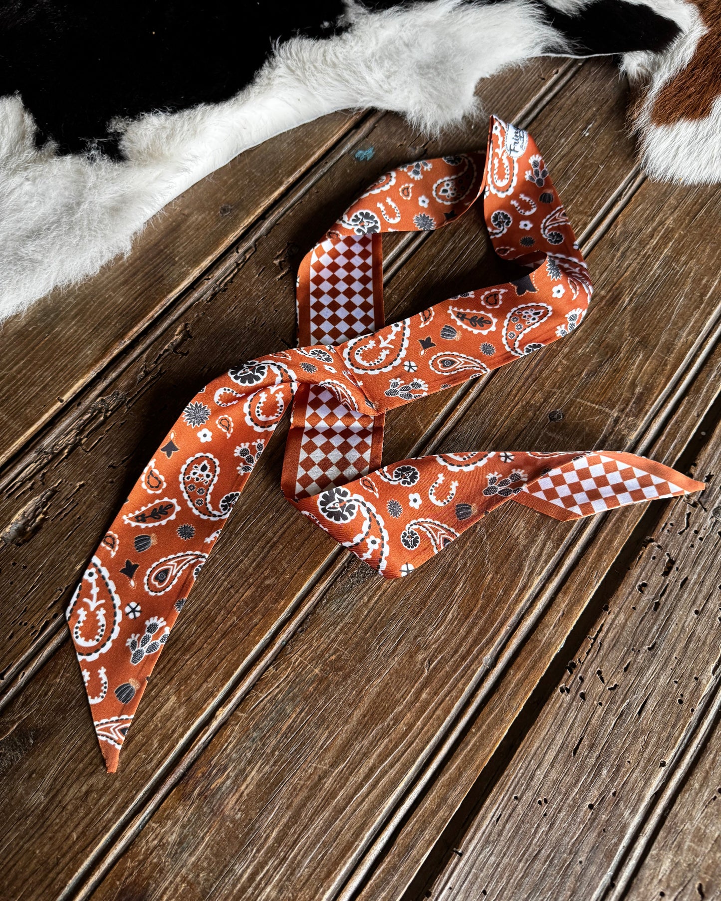 Orange paisley scarf on a wooden surface with cowhide rug in the background