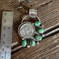 Silver brooch with green gemstones on a wooden surface with a ruler for scale.