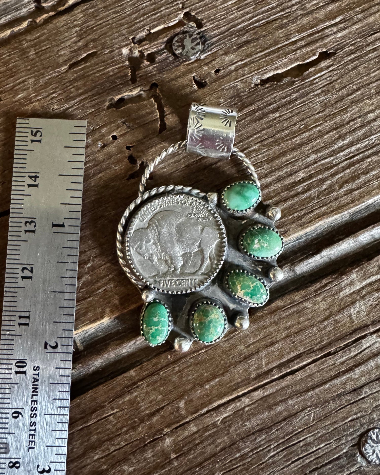 Silver brooch with green gemstones on a wooden surface with a ruler for scale.
