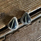 Triangular earrings with black stones and silver accents on a wooden surface