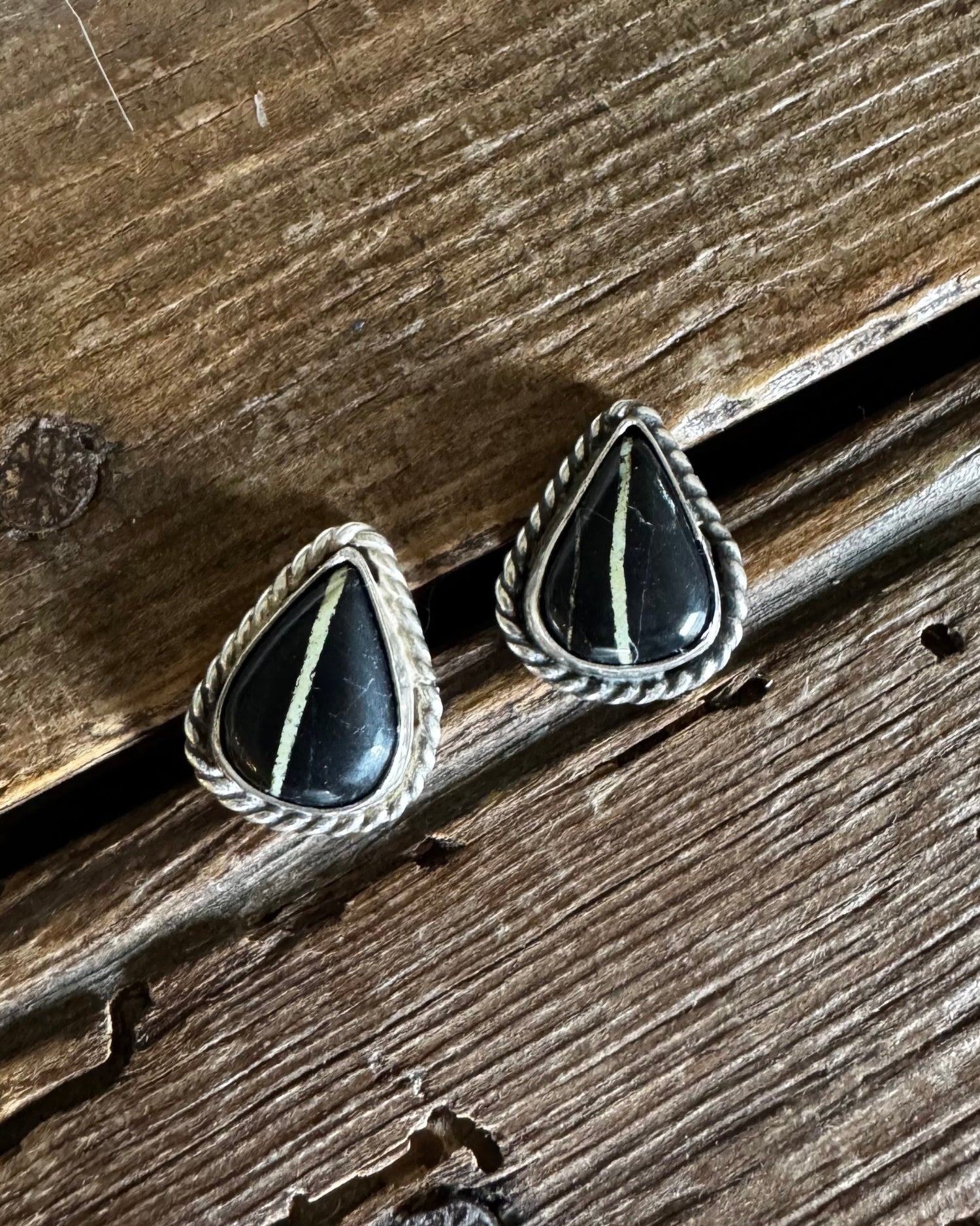 Triangular earrings with black stones and silver accents on a wooden surface