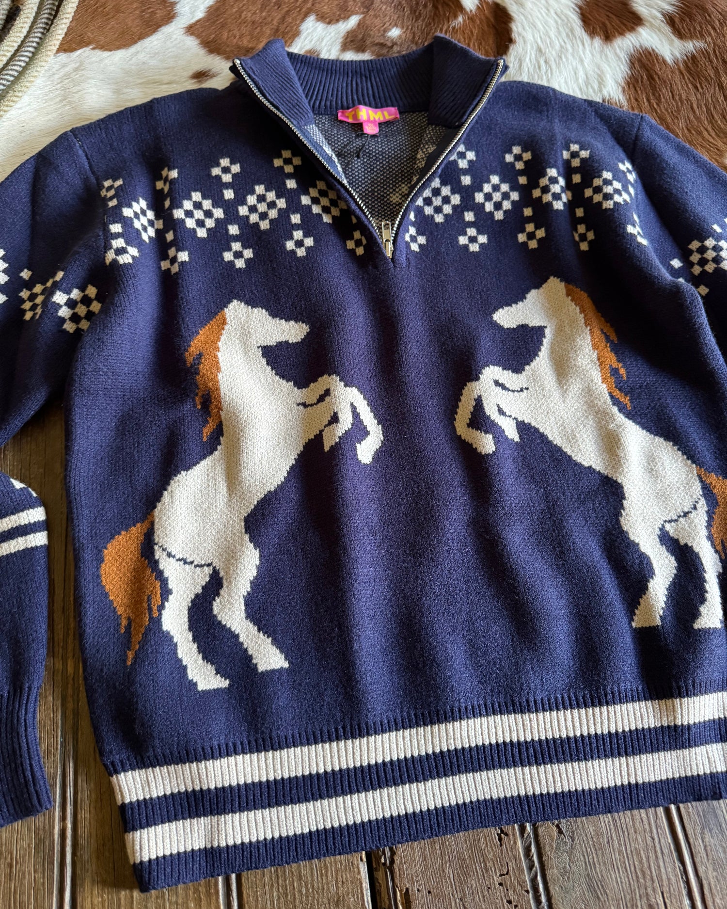 Navy blue sweater with horse design on a wooden surface