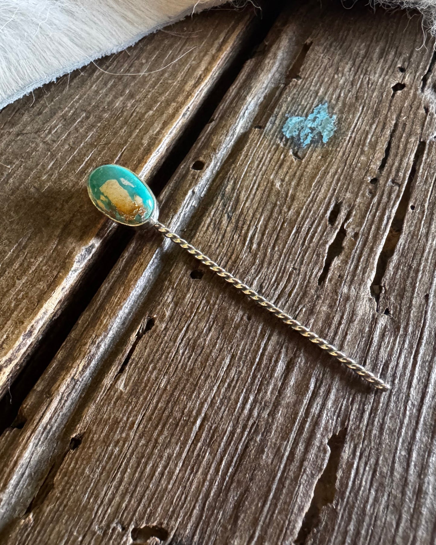 Teal pin with a decorative head on a wooden surface