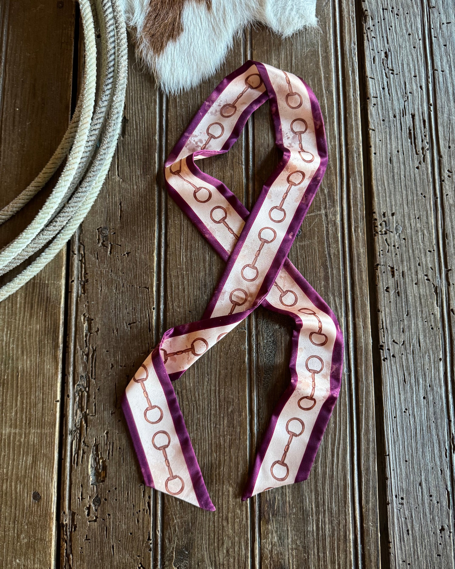 Snaffle bit ribbon scarf on a rustic wooden background with a rope