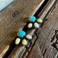 A pair of silver stud earrings with turquoise blue square centers and small cream-colored oval stones, displayed on a rustic wooden surface next to a white faux fur fabric.