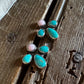 A pair of handmade turquoise and pink stone stud earrings in silver settings, displayed on a rustic wooden surface next to a white fur trim.